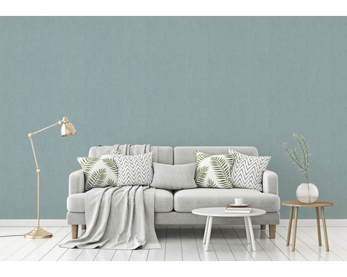 Woonkamer met lichtblauw structuurbehang, bank, tafel en staande lamp.