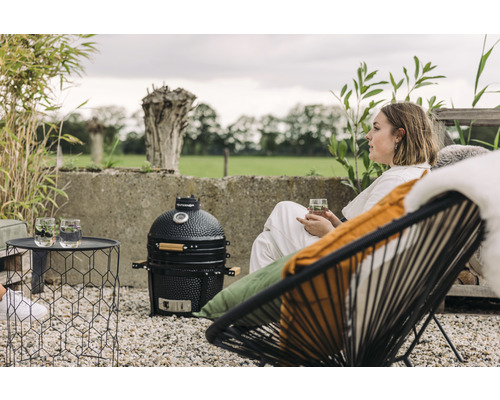 Buitenscène met een keramische barbecue, een bijzettafel met drankjes en een vrouw die in een stoel zit.