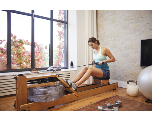 Vrouw gebruikt roeimachine in een lichte kamer met sporttoestellen.