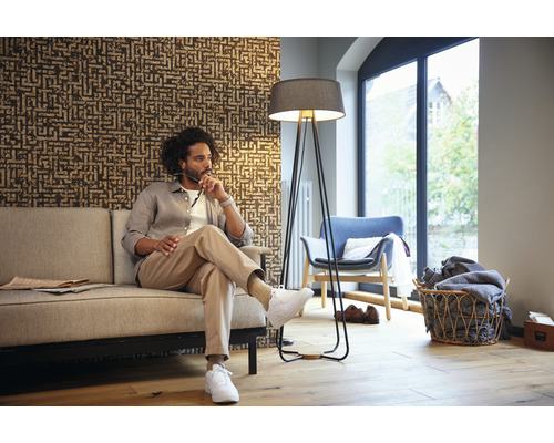 Woonkamer met man op de bank, staande lamp en patroonbehang