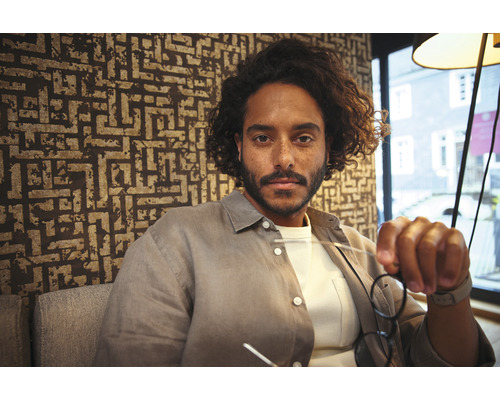 Portret van een man met een bril voor een muur met patroon