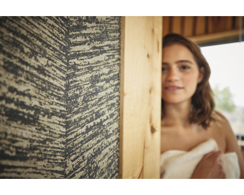 Close-up van een vrouw met een handdoek om zich heen, naast een gestructureerde wand in een ruimte met houten accenten.