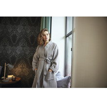 Vrouw met grijze wafelbadjas in een kamer met behang met patroon