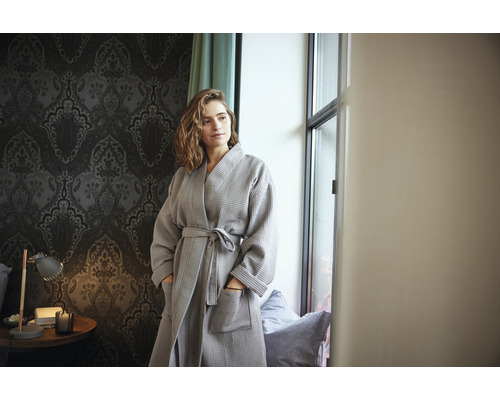 Vrouw met grijze wafelbadjas in een kamer met behang met patroon