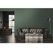 Woonkamer met leren bank, tafel en vloerlamp tegen een muur met behang.