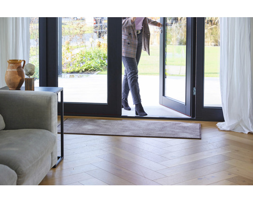 Entree met deurmat, houten vloer en een vrouw die door een deur loopt