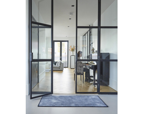 Interieurfoto van een woonkamer met glazen deuren, tapijt en een persoon achter een piano.