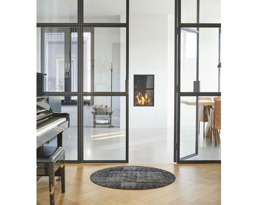 Woonkamer met glazen schuifdeuren, open haard, piano en rond vloerkleed op houten vloer.