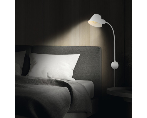 Slaapkamer met bed en een witte wandlamp.