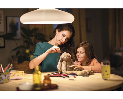 Moeder en dochter zitten aan een tafel onder een lamp en naaien een knuffel.