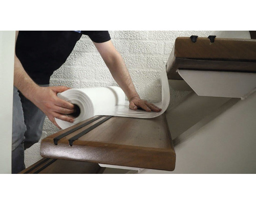 Ambachtsman rolt trapbeschermfolie uit op een houten trap.