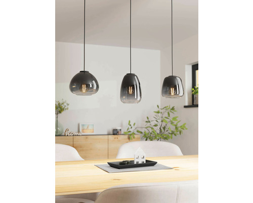 Drie grijze hanglampen met verschillende vormen boven een houten tafel