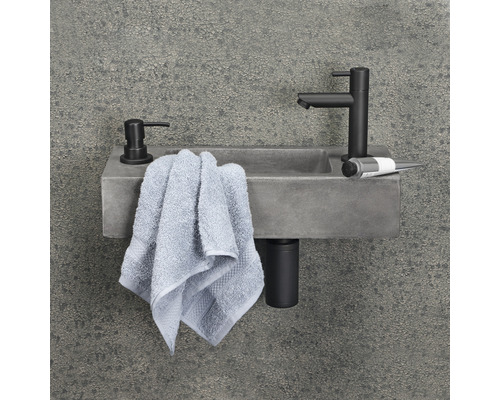 Betonnen wastafel in badkamer met kraan, zeepdispenser en handdoek