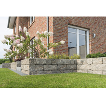 Buitenfoto van een tuin met een droge muur van granieten stenen voor een huis met bakstenen muren