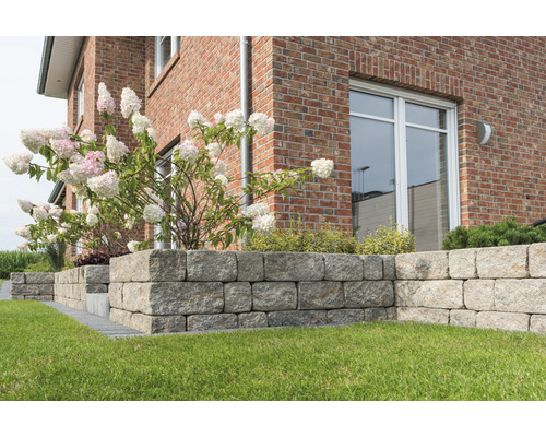 Buitenfoto van een tuin met een droge muur van granieten stenen voor een huis met bakstenen muren