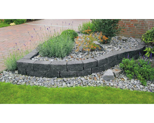 Tuinontwerp met een muur van grijze betonblokken, omgeven door planten en stenen.