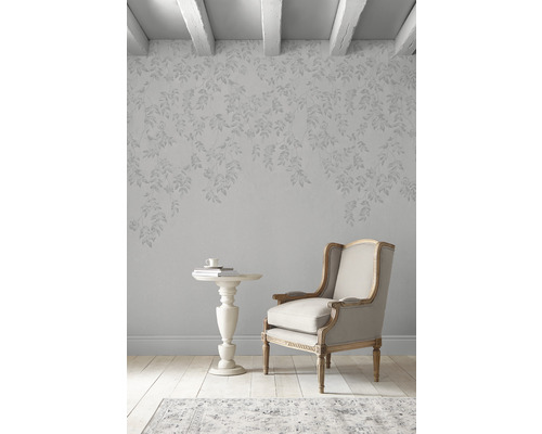 Interieurscène met fauteuil, bijzettafel en behang met bladerpatroon in een lichte kamer.