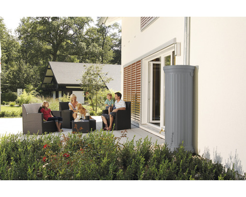 Familie zit op het terras naast een grijze regenwatertank bij het huis.