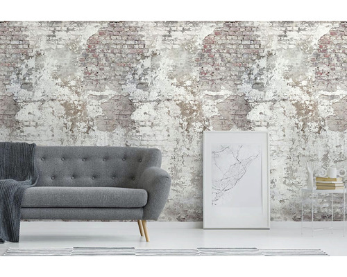 Woonkamer met grijze bank voor een behang dat een afbrokkelende bakstenen muur imiteert.