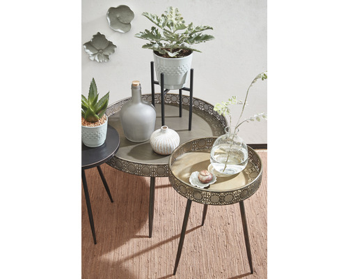 Decoratieve scène met diverse bijzettafels, planten en vazen op een vloerkleed.