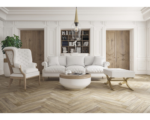 Woonkamer met bank, fauteuil, voetenbank, salontafel en boekenkast in een lichte kamer.