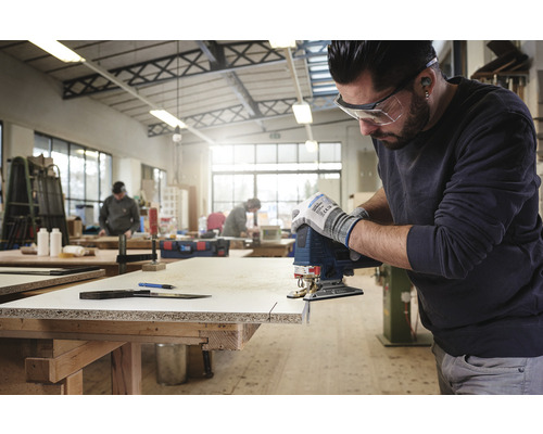 Een man zaagt een werkstuk met een decoupeerzaag in een werkplaats.