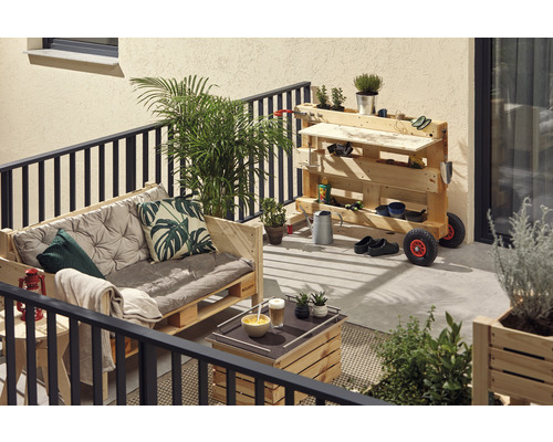 Balkon met houten meubels gemaakt van pallets, waaronder een bank met kussens, een tafel en een mobiele werkbank met tuingereedschap.