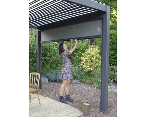 Vrouw bedient een uitschuifbaar zijscherm op een aluminium terrasoverkapping.