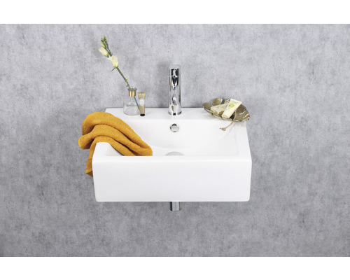 Kleine wastafel met kraan, handdoek en decoratie tegen een grijze muur