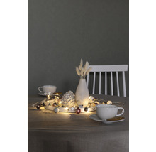 Decoratie met lichtsnoer, dennenappel, vaas en kopjes op een tafel