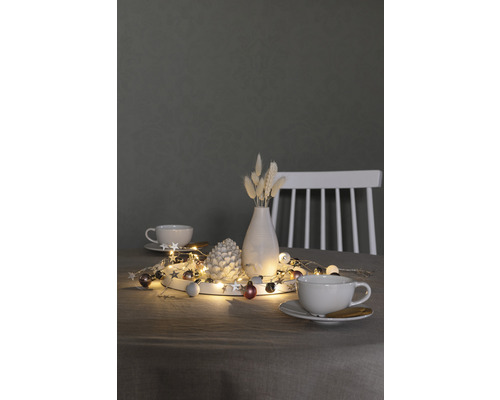 Decoratie met lichtsnoer, dennenappel, vaas en kopjes op een tafel