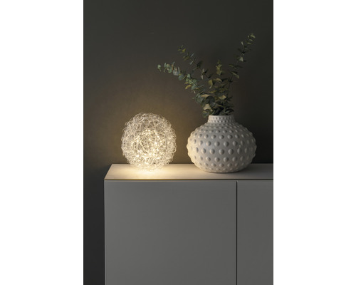 Decoratieve bolvormige tafellamp naast een vaas met planten op een kast