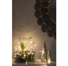 Decoratieve glazen pot met hyacint, mos, ballen en lichtsnoer, naast decoratieve keramische bomen en een ronde spiegel