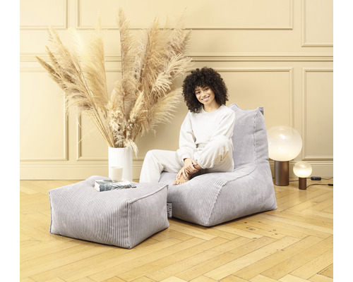 Vrouw zit in een kamer op een grijze corduroy zitzak met bijpassende kruk