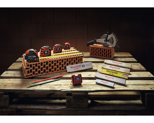 Metselwerkgereedschapassortiment op houten pallet met rolmaten, meetwiel, vouwmeter, potloden en digitale klok