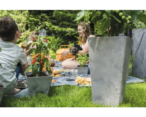 Familie tuinscène met betonnen plantenbakken, picknickkleed en mensen