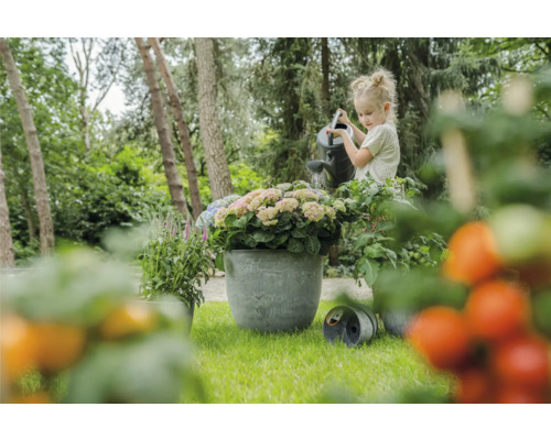 Meisje geeft bloemen in plantenbak water met gieter in de tuin
