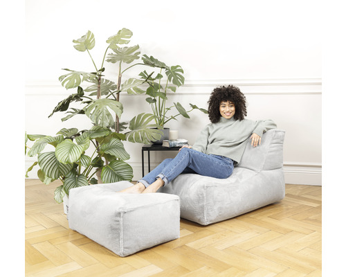 Vrouw ontspant op fauteuil met voetenbank in de woonkamer met planten