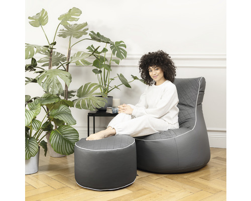 Vrouw zit op een grijze zitzak met voetenbank in de woonkamer.