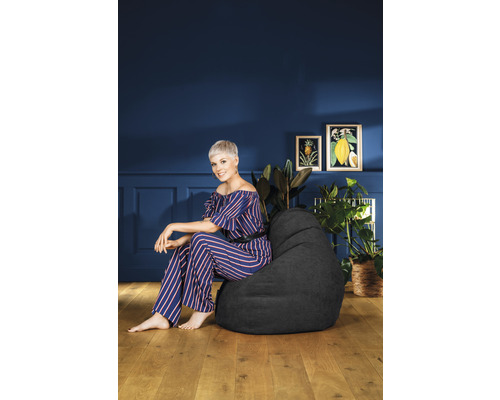 Vrouw zit op een zwarte zitzak in een woonkamer met planten en kunst aan de muur