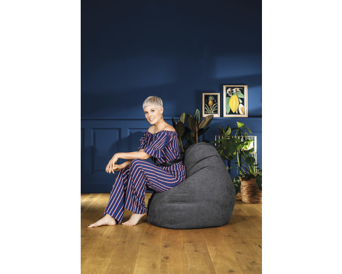 Vrouw zit op een grijze zitzak in een woonkamer met planten en decoratie