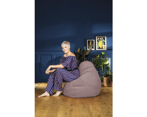 Vrouw zit op een grijze zitzak in een woonkamer.