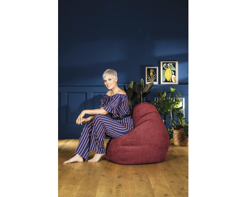 Vrouw zit op een bordeauxrode zitzak in de woonkamer voor een blauwe muur met decoratie