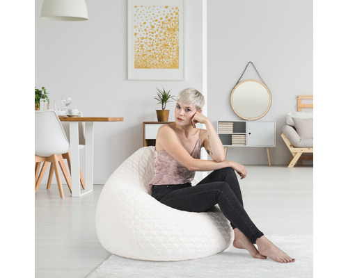 Een vrouw zit op een witte zitzak in een lichte woonkamer.