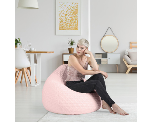 Vrouw zit op een roze zitzak in een lichte woonkamer.