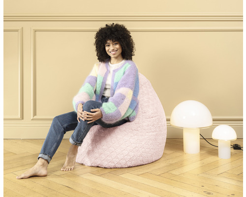 Vrouw zit op een roze zitzak naast twee lampen in paddenstoelvorm