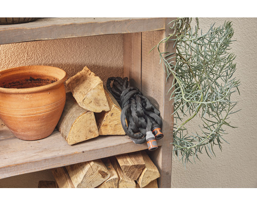 Houten rek met bloempot, brandhout, tuinslang en groene plant