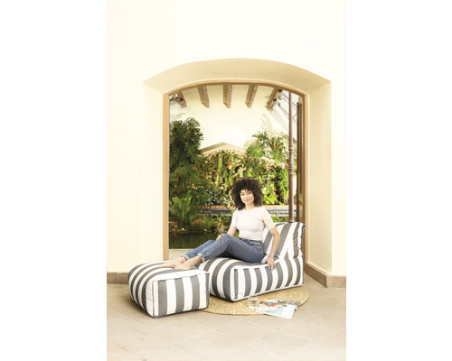 Scène met een vrouw zittend op een gestreepte zitzak met voetenbank op een rond vloerkleed