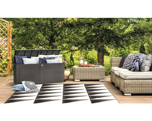 Tuinscene met een kussenbox, een tafel, een bank en een vloerkleed op een houten terras