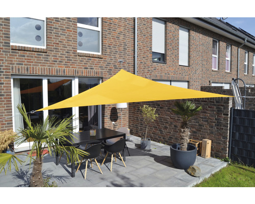 Geel driehoekig zonnescherm boven een terras met tafel en stoelen voor een woonhuis.